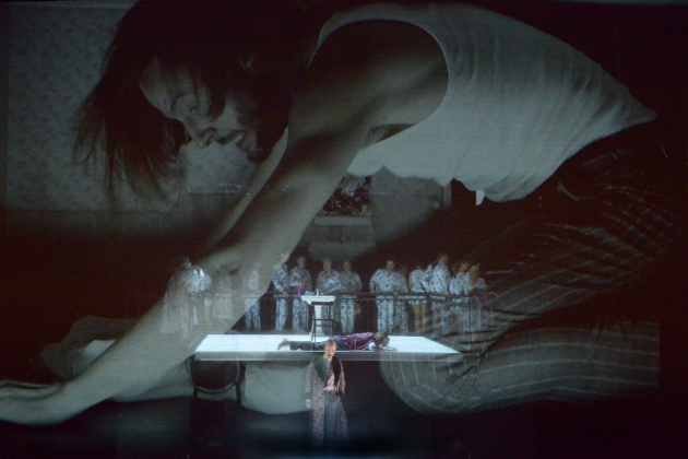 Alfred Reiter (Herr Zenk, standing), Björn Bürger (Georg, lying down and on big screen) and chorus