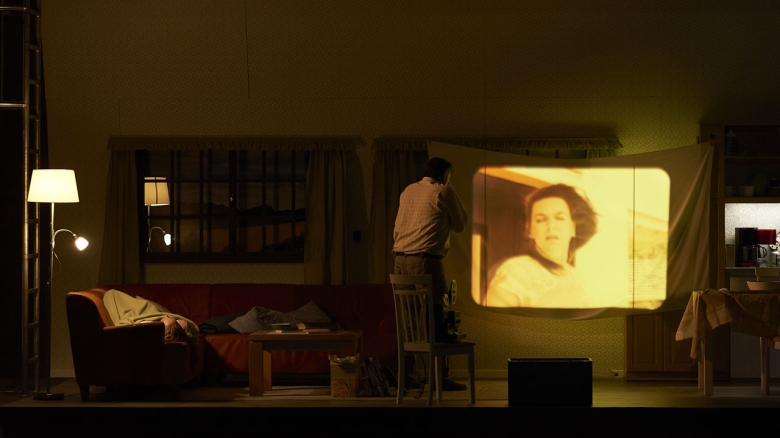  Iain MacNeil (Kajin; auf dem Sofa liegend) und Andreas Bauer Kanabas (Adahm; vor der Leinwand), Ambur Braid (Chawa; im Film)