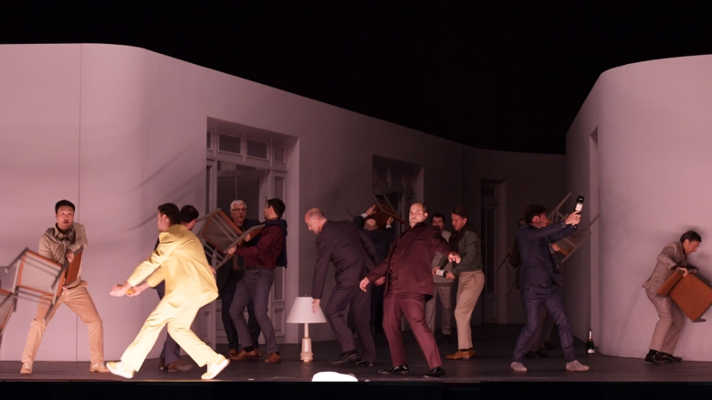 Danylo Matviienko (Papageno; in gelbem Anzug), Michael McCown (Erster geharnischter Mann; in schwarzem Anzug), Theo Lebow (Monostatos; in rotem Anzug), Chor der Oper Frankfurt